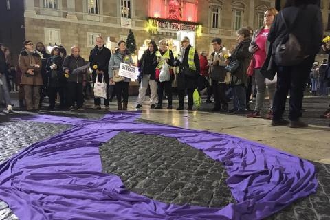 Imatge d'una concentració a la plaça Sant Jaume amb diverses persones al voltant d'un llaç lila de tela posat a terra